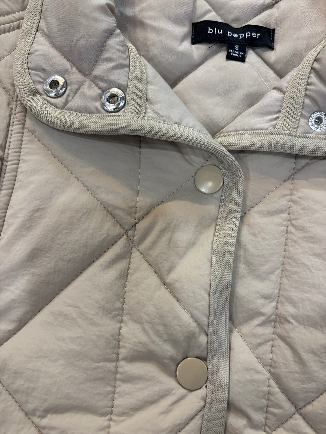 Close-up of cream quilted vest collar, snap buttons, diamond stitching and label
