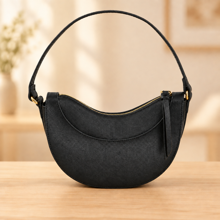 Black crescent bag with short shoulder strap on a warm wooden table against a soft neutral background