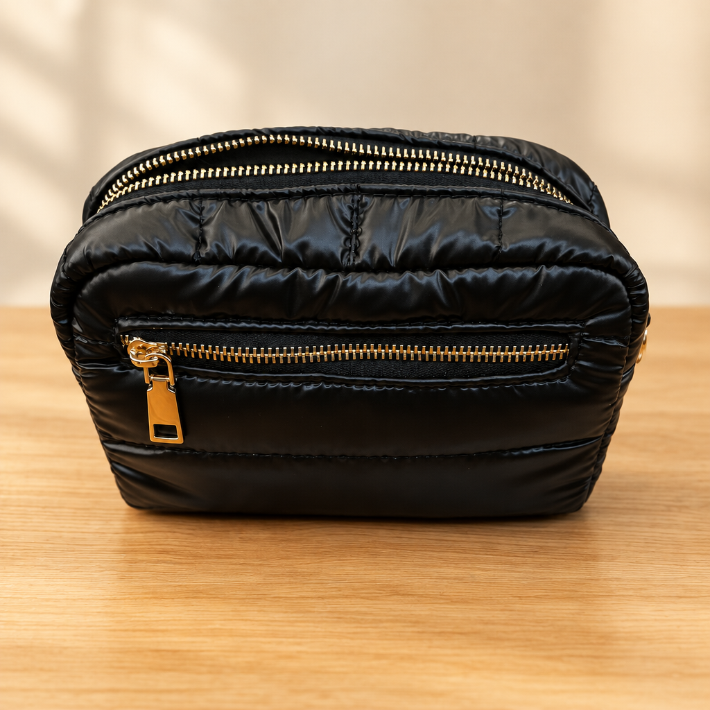 Black quilted zippered bag with gold hardware on a warm wooden table against a soft neutral background
