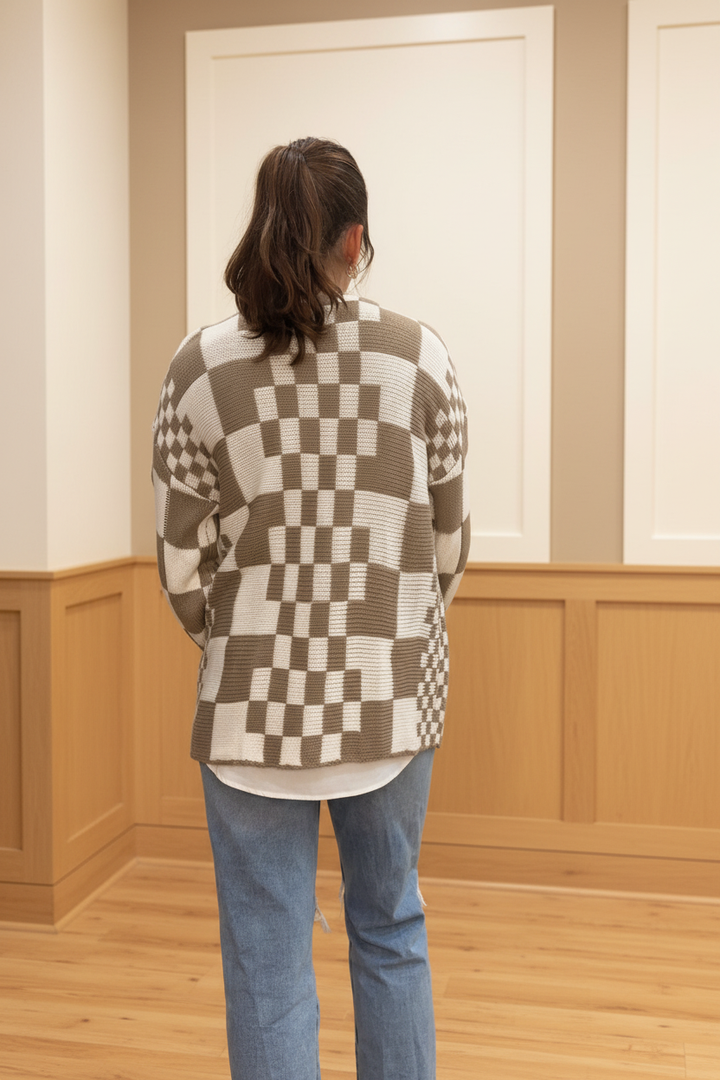 Model wearing a taupe and ivory mixed checkered open-front cardigan in a warm neutral boutique setting, back view