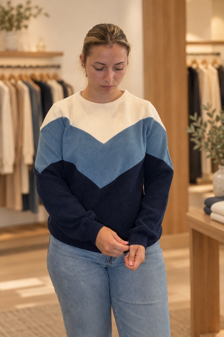 Model wearing a cream, steel blue, and navy diagonal color block sweater in a warm modern boutique