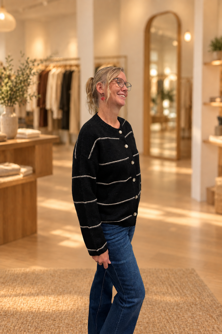 Side view of black thin-striped button cardigan modeled in a warm boutique