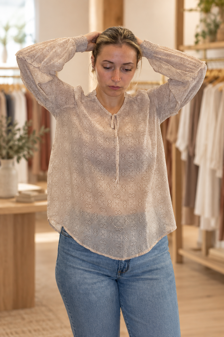 Model wearing a blush mixed floral smocked tier sleeve blouse in a warm modern boutique, front view