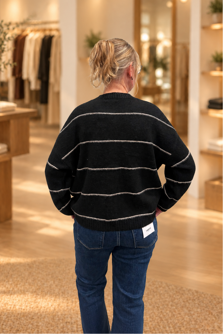 Back view of black thin-striped button cardigan modeled in a warm boutique
