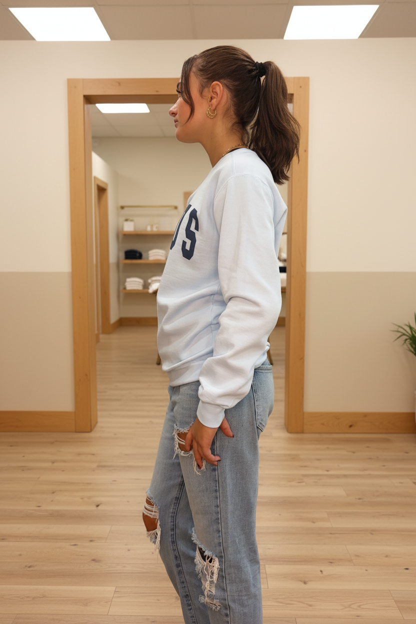 Model wearing the light blue Jesus arch lettering crewneck sweatshirt in a warm neutral boutique setting, side view