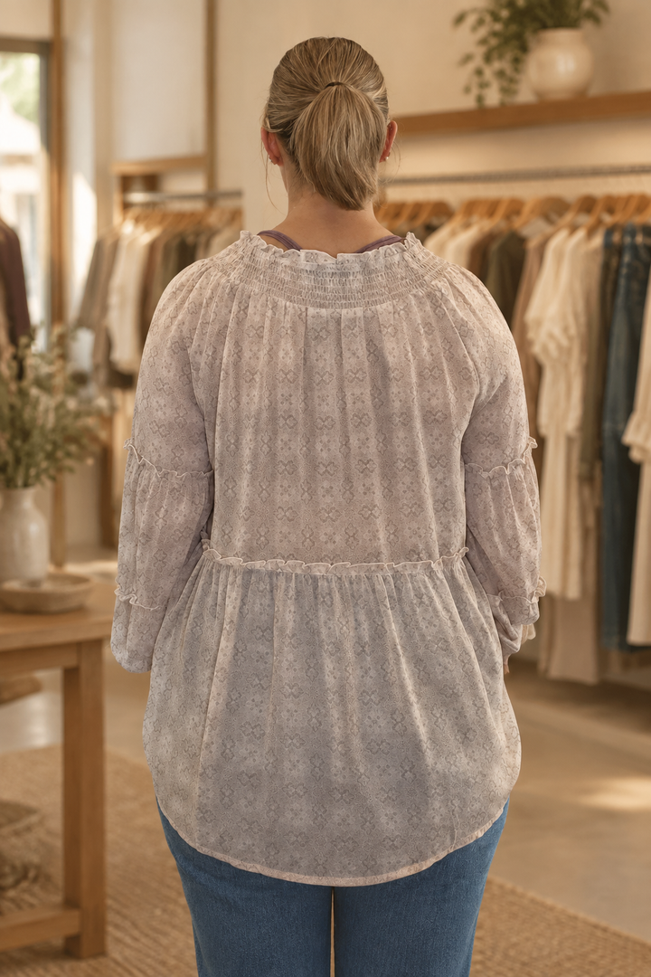 Back view of model wearing a blush mixed floral smocked tier sleeve blouse in a warm modern boutique