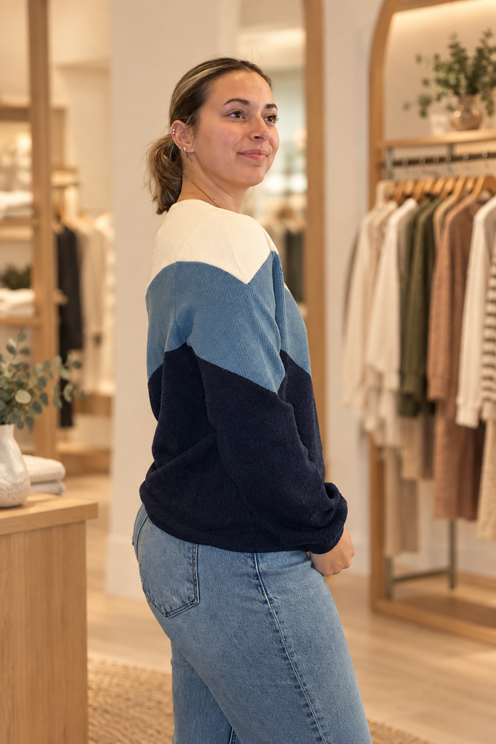 Side view of model wearing a cream, steel blue, and navy color block sweater in a warm modern boutique