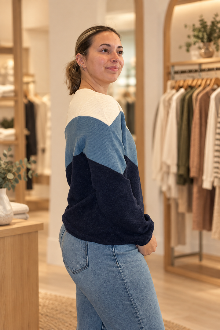 Side view of model wearing a cream, steel blue, and navy color block sweater in a warm modern boutique