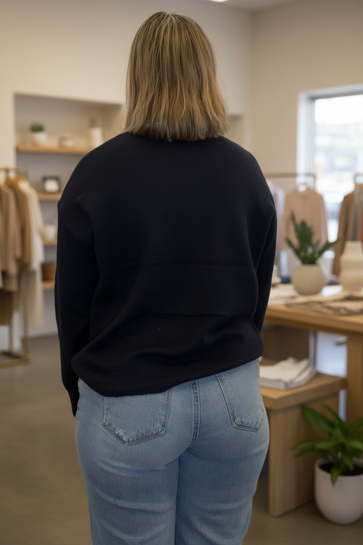 Back view of a plain navy cowboy boots graphic pullover sweater in a warm boutique setting