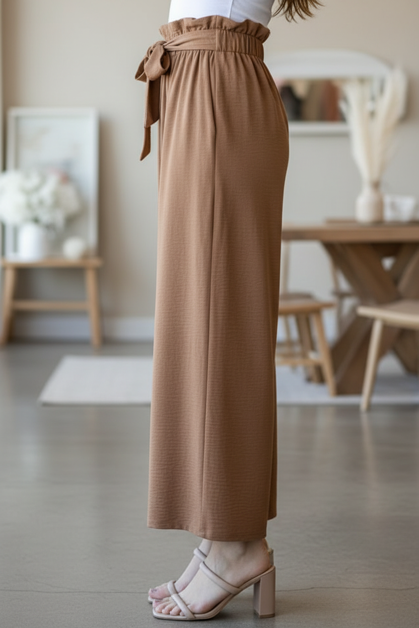 Wide-leg taupe paper bag pants side view on model with soft neutral blurred boutique background
