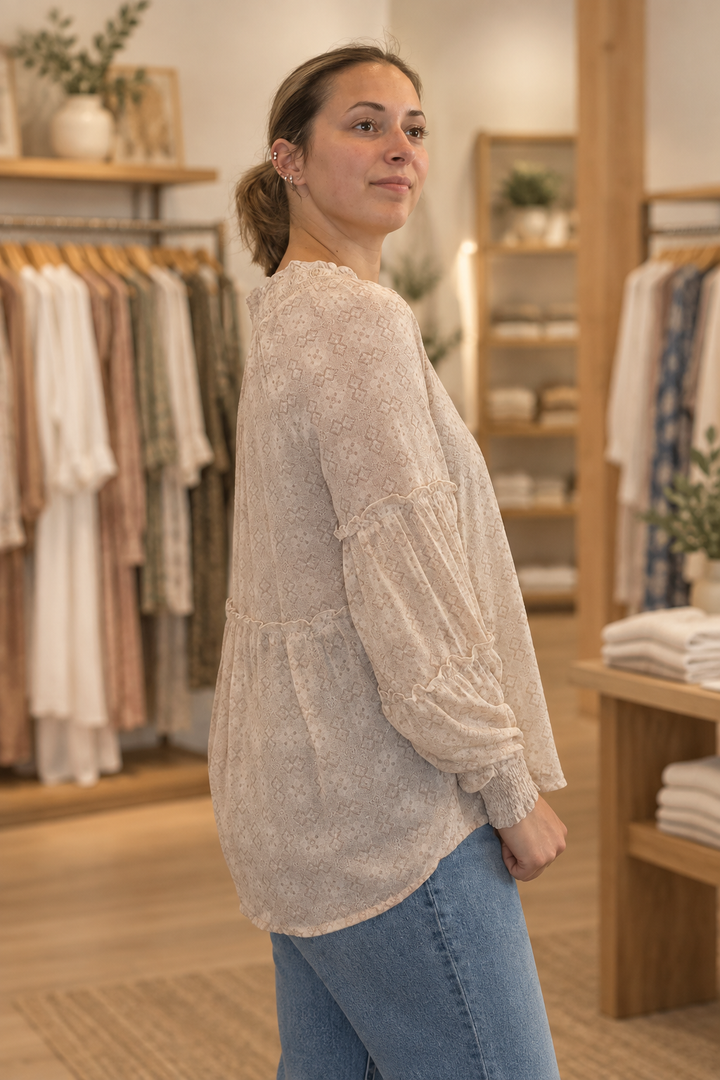 Side view of model wearing a blush mixed floral smocked tier sleeve blouse in a warm modern boutique