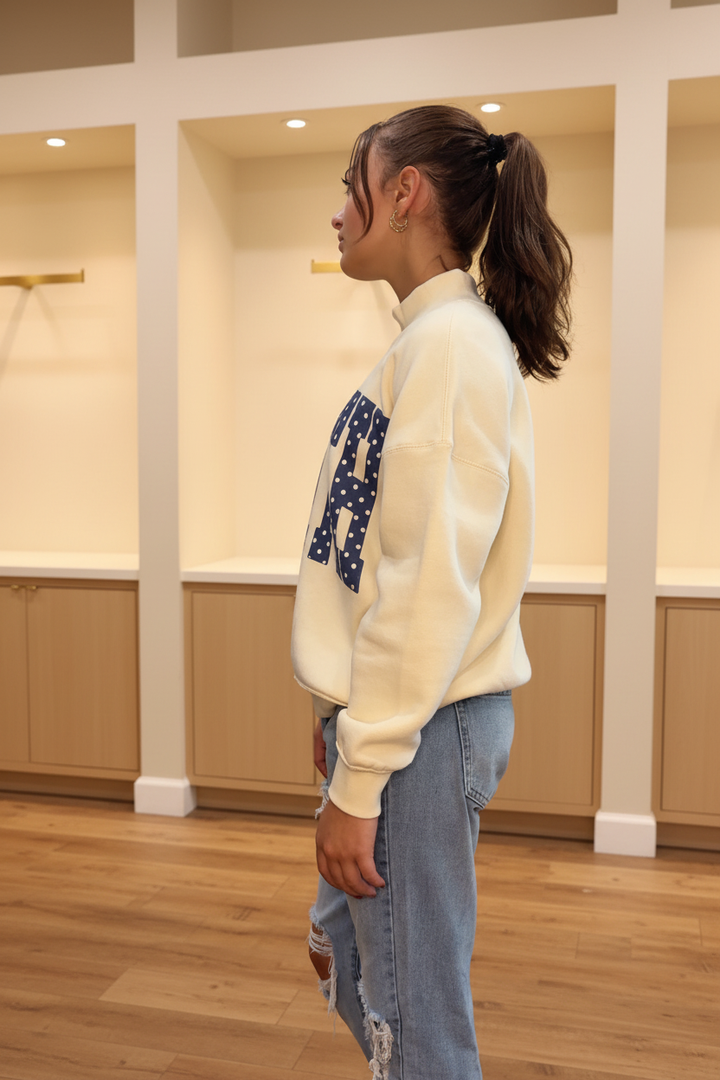 Model wearing the cream Faith polka dot mockneck sweatshirt in a warm neutral boutique setting, side view