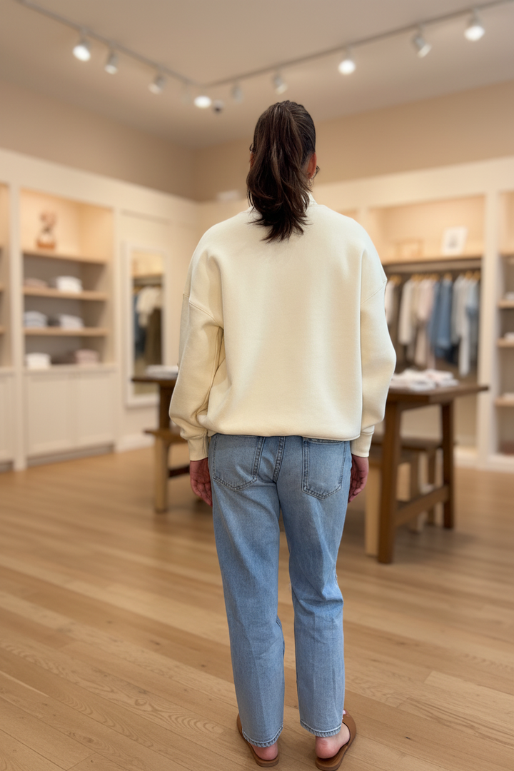 Model wearing the cream Faith polka dot mockneck sweatshirt in a warm neutral boutique setting, back view with plain sweatshirt back