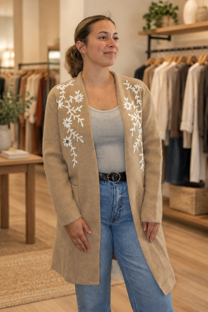 Model wearing a tan floral embroidered longline coatigan in a warm modern boutique, front view