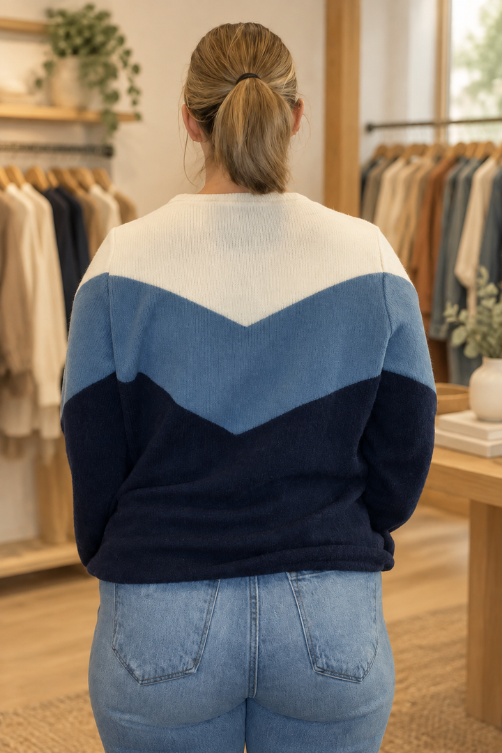Back view of model wearing a cream, steel blue, and navy color block sweater in a warm modern boutique