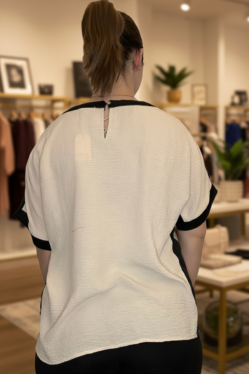Cream and black colorblock dolman sleeve top side view with blurred boutique background