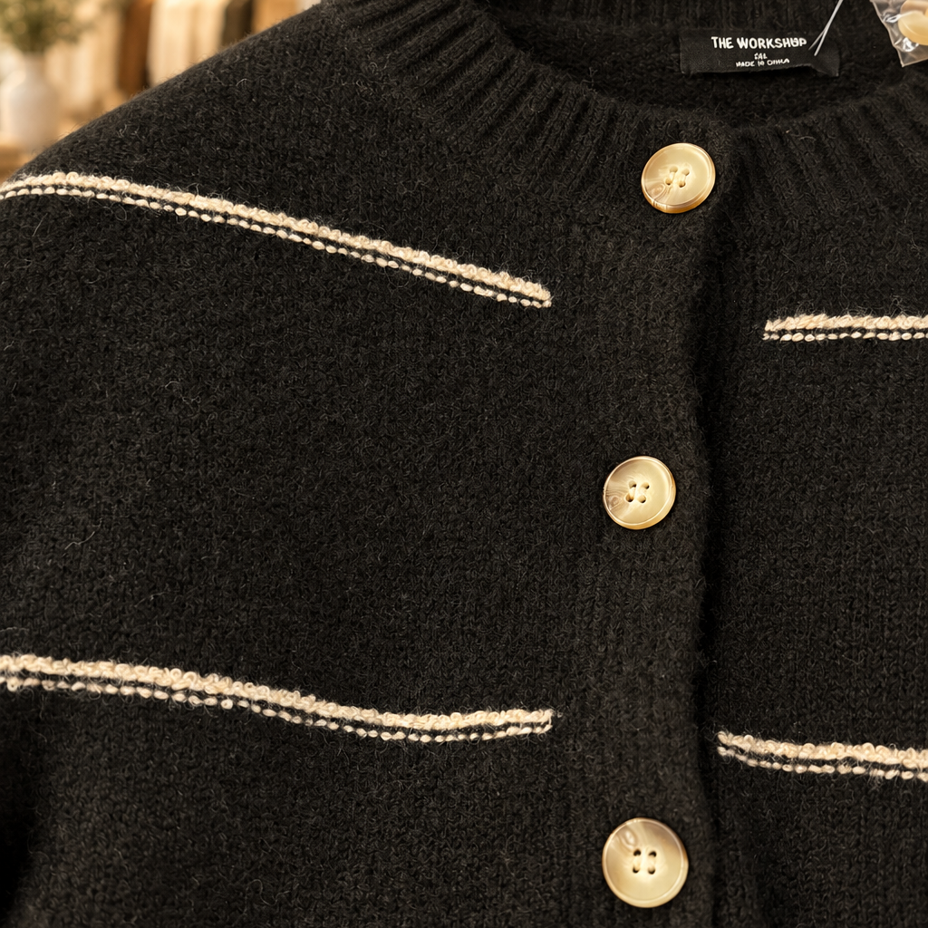 Close-up of black cardigan knit, cream stripes and buttons with boutique shelves behind
