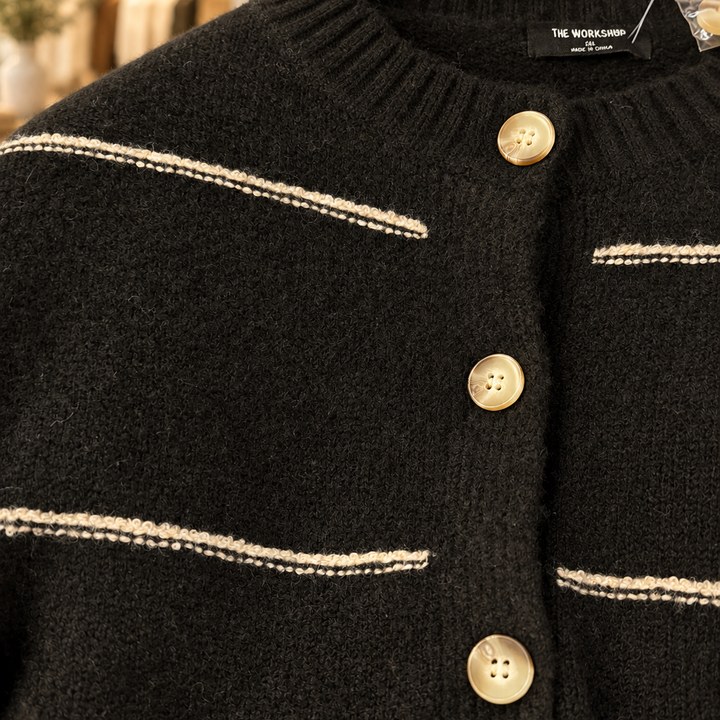 Close-up of black cardigan knit, cream stripes and buttons with boutique shelves behind