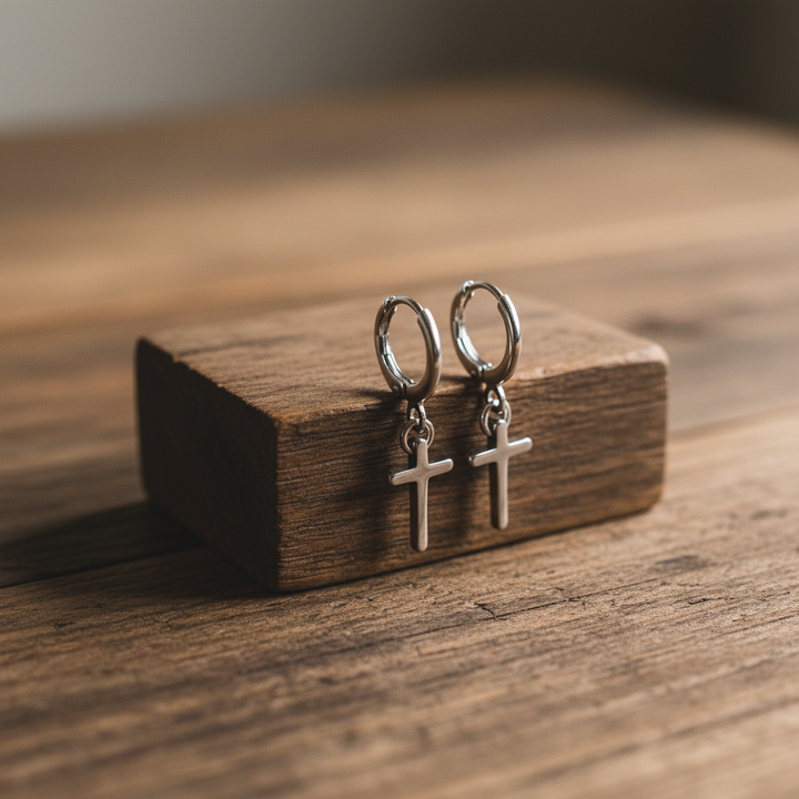 Silver cross huggie earrings propped on a wooden table