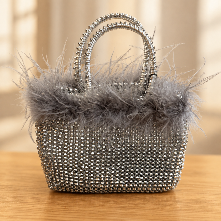 Silver rhinestone handbag with gray feather trim on a warm wooden table against a soft neutral background